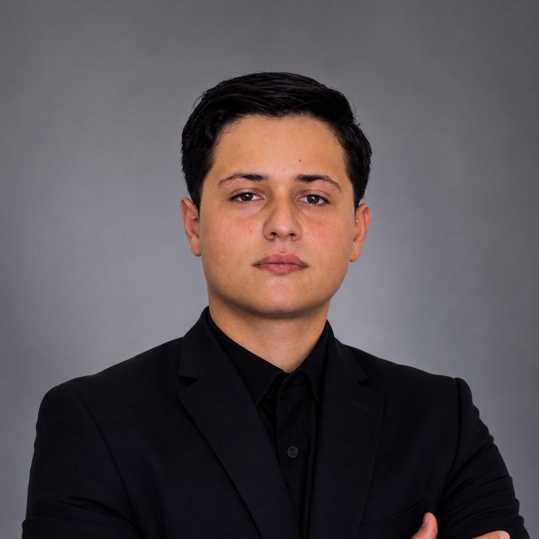 Julián con traje negro y brazos cruzados frente a un fondo gris